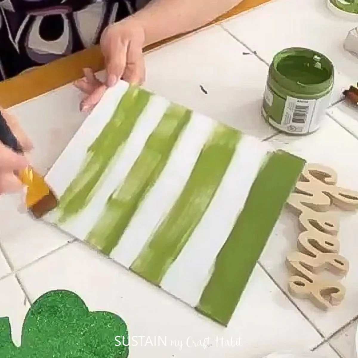 Adding strips of green paint to a canvas board.