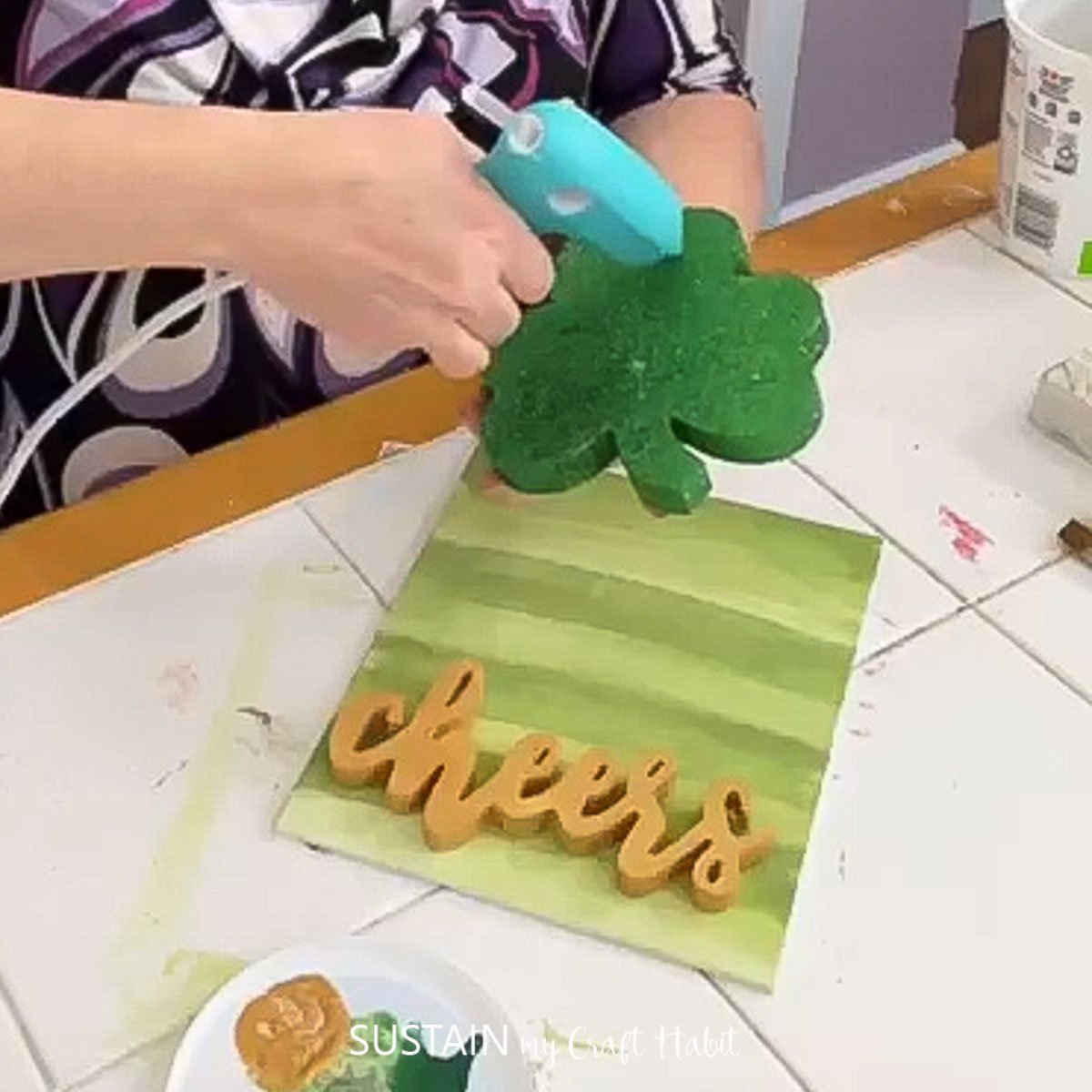 Adding hot glue to a glitter shamrock.