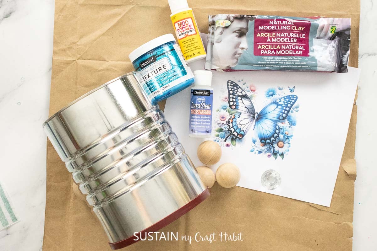 Materials needed to craft a coffee tin planter including a coffee tin, paint, paintbrushes, picture and glue.