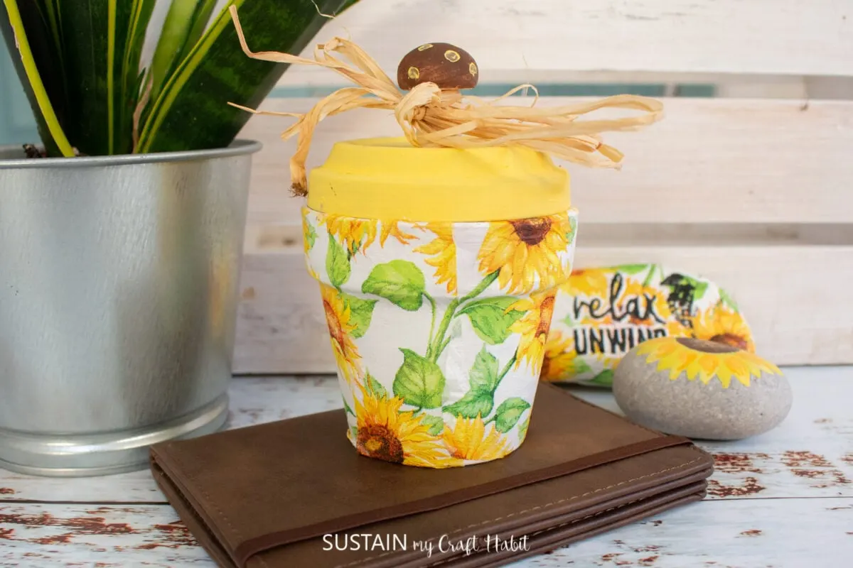 Decoupage clay pot decorated with decorative sunflower napkins, yellow paint and raffia ribbon.