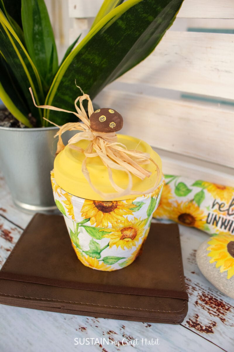 Decoupage clay pot decorated with decorative sunflower napkins, yellow paint and raffia ribbon.