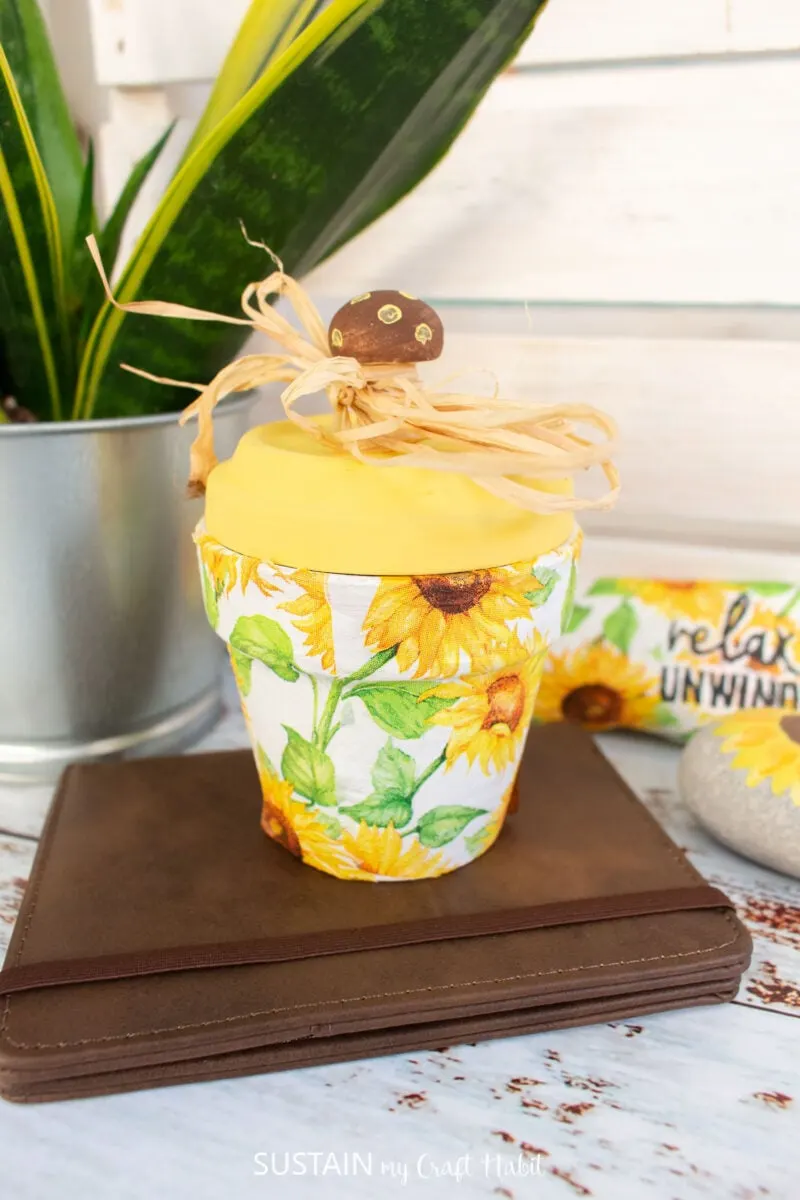 Decoupage clay pot decorated with decorative sunflower napkins, yellow paint and raffia ribbon.