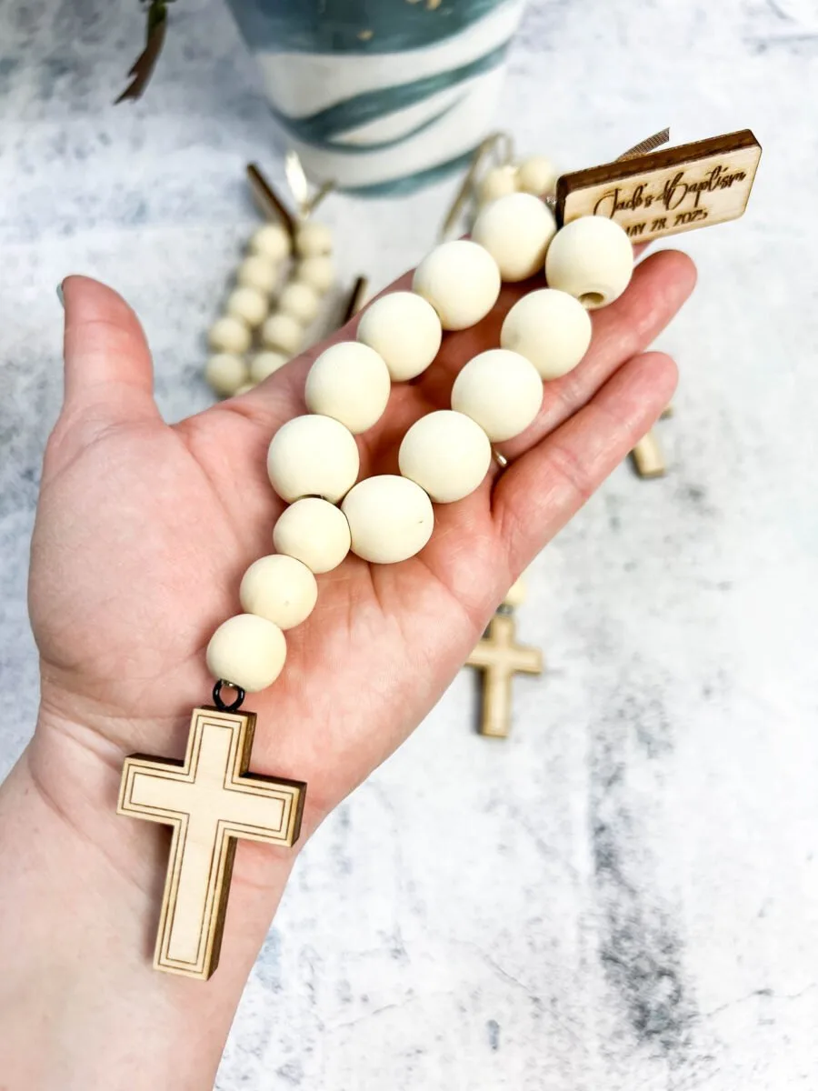 Hand holding a wooden bead rosary baptism favor.