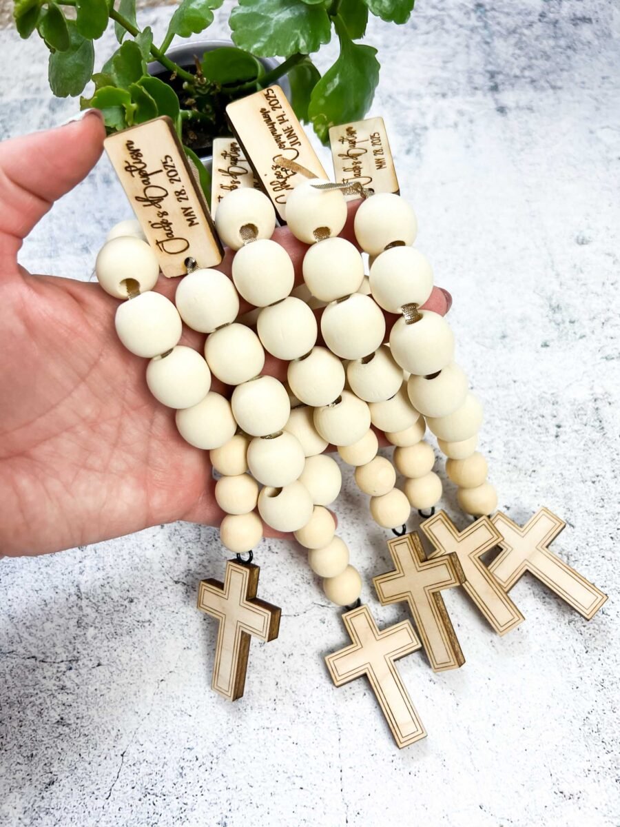 Hand holding wooden bead rosaries baptism favors.
