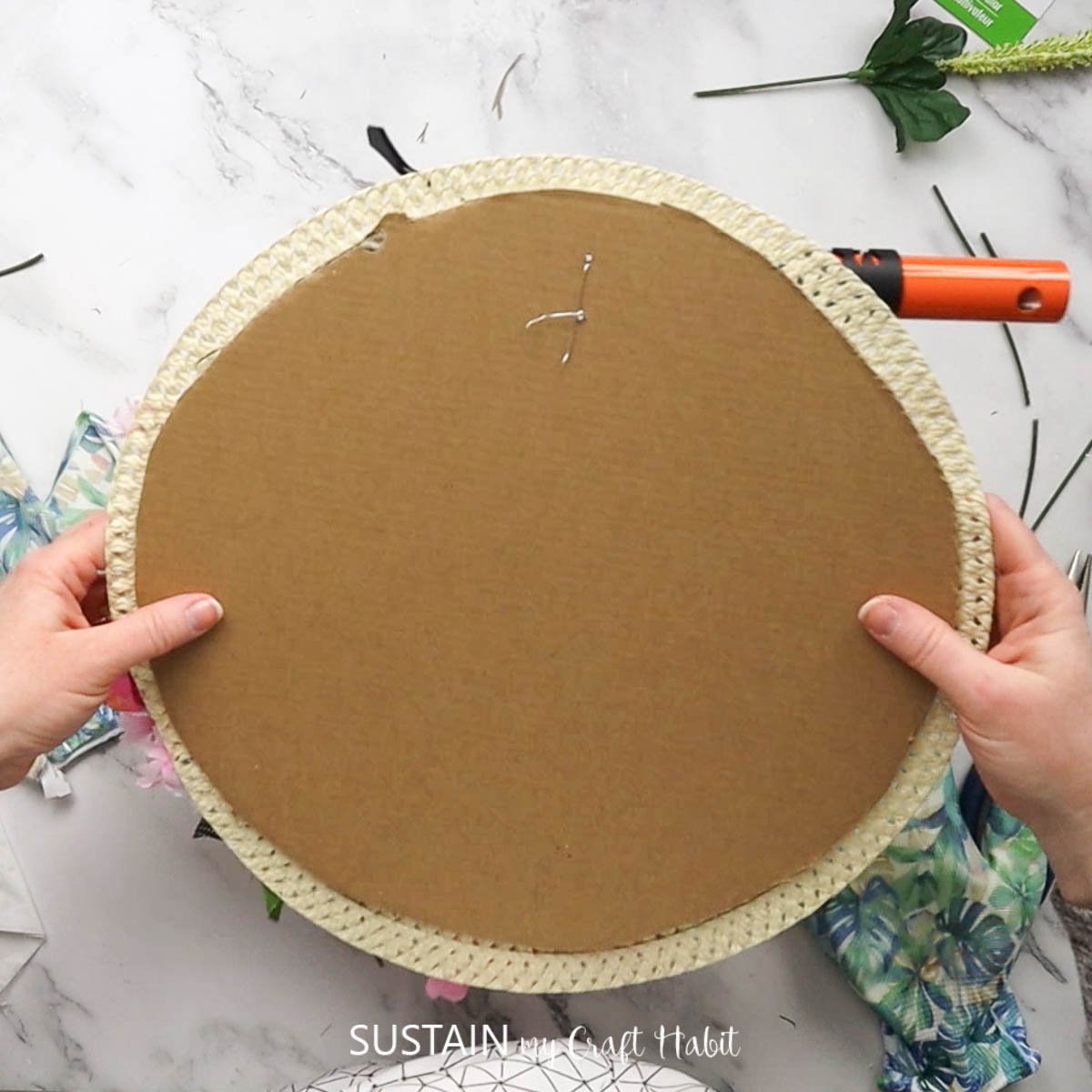 Attaching a straw hat to cardboard.