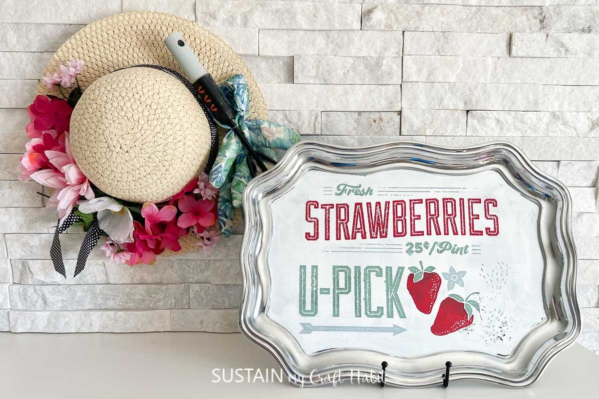 Chalk Couture strawberry stencil on a painted silver tray displayed next to a summer hat.