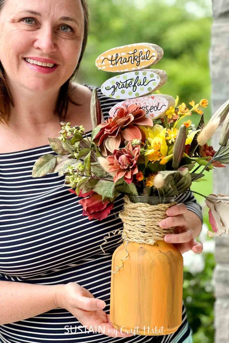 Woman holding a mason jar pumpkin filled with flowers.