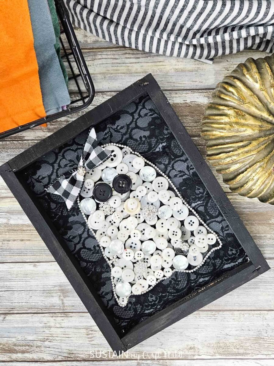 Ghost art made from buttons that are glued onto a lace background.