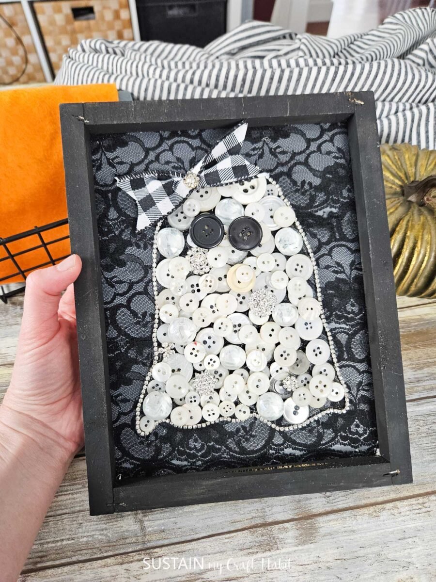 Ghost art made from buttons that are glued onto a lace background.
