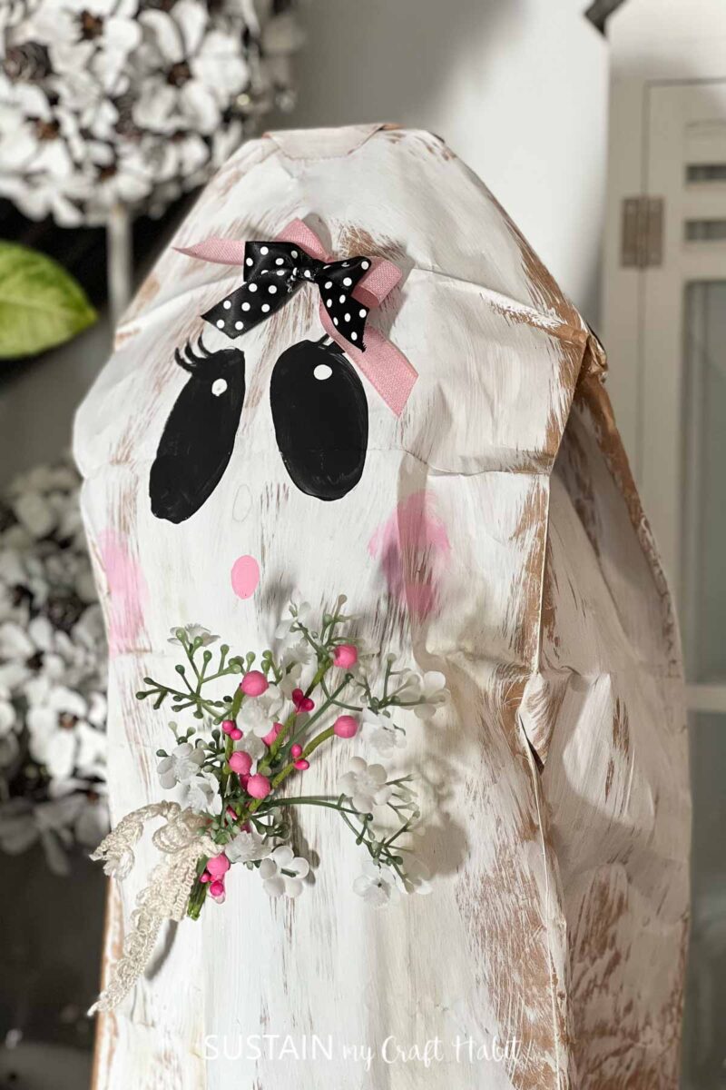 Paper bag ghost painted and embellished with ribbon and flowers.