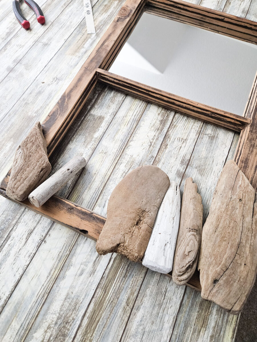 Layering driftwood pieces onto a mirror frame.