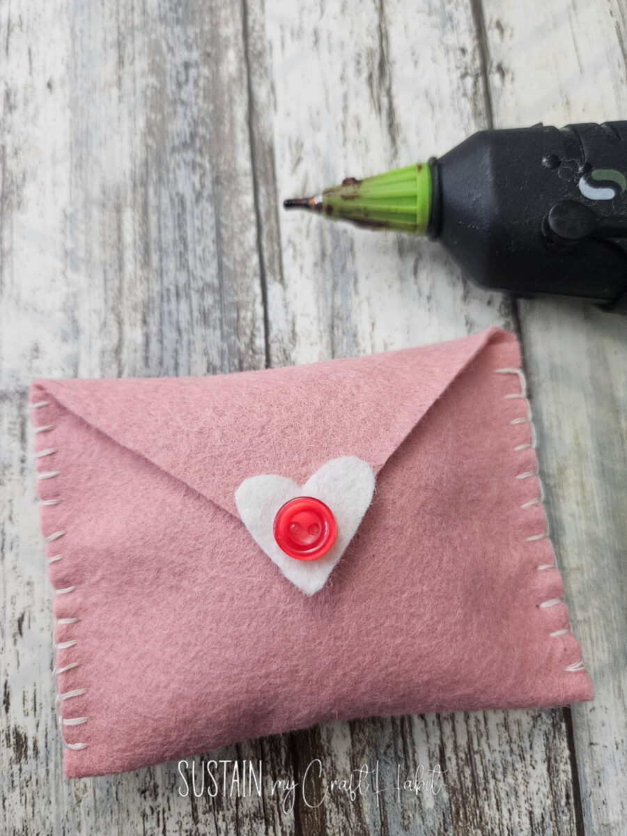 Hot gluing a heart shape and button to the felt fabric envelope.