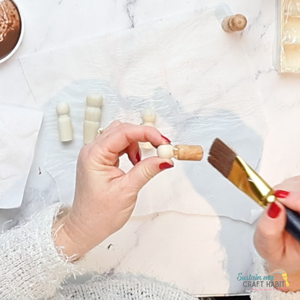 Painting a wooden peg with brown paint.