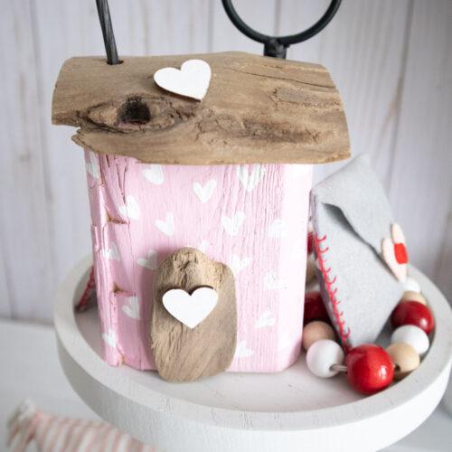 Small pink house made from scrap wood styled on a white tiered tray.