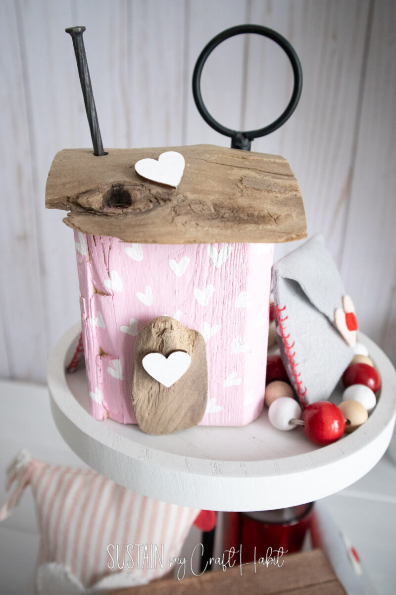 Small pink house made from scrap wood styled on a white tiered tray.