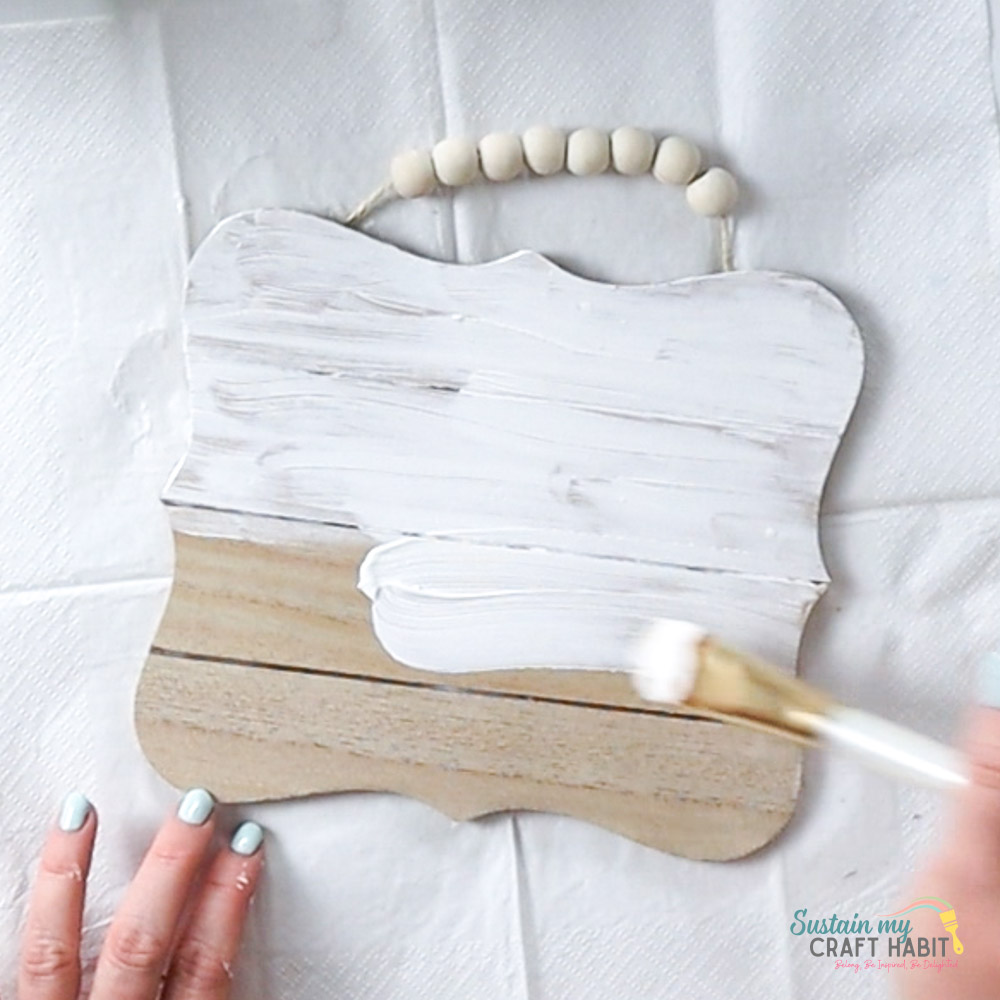 Painting a wooden plaque with white paint.