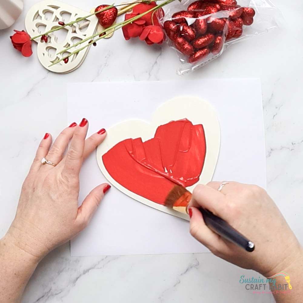 Painting a wooden heart with red paint.