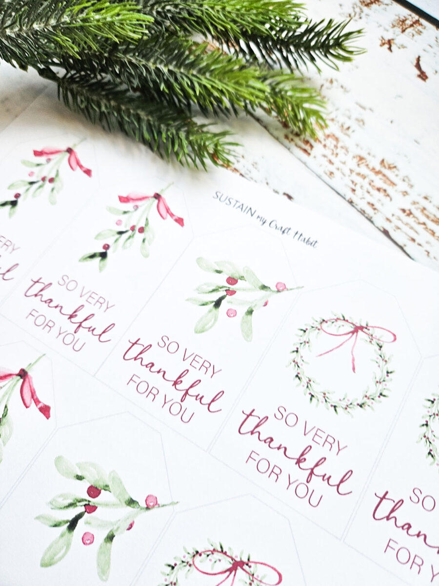 Printable holiday gift tags beside a sprig of greenery.
