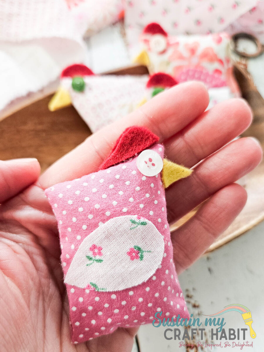 Hand holding a scrap fabric chicken pocket buddy. 