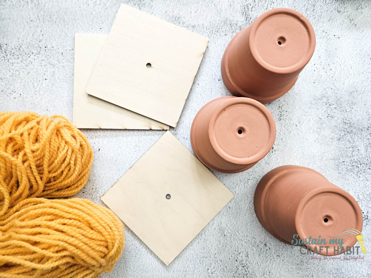 Materials needed to make graduation cap decor including terracotta pots, wood slices and yellow yarn.