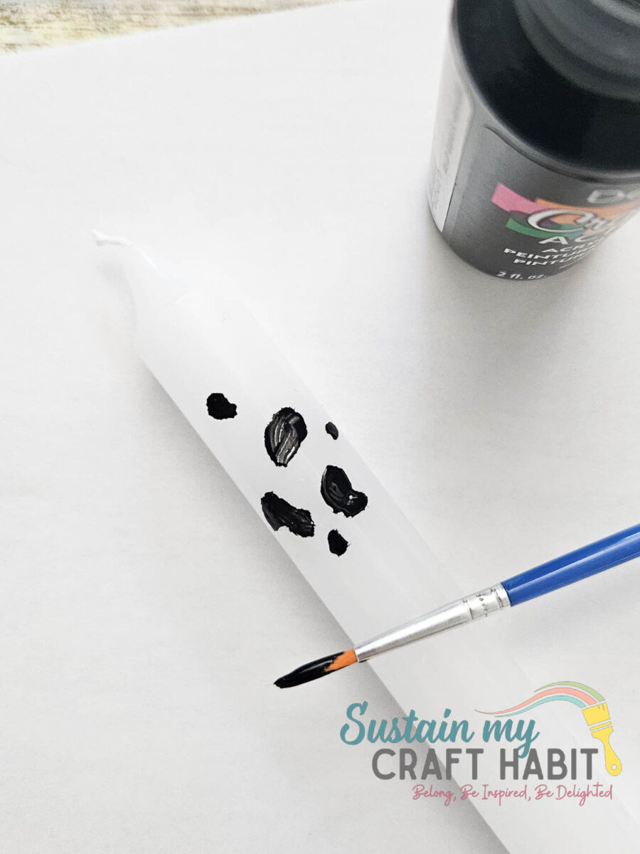 painting black geometric dalmatian shapes on a candle