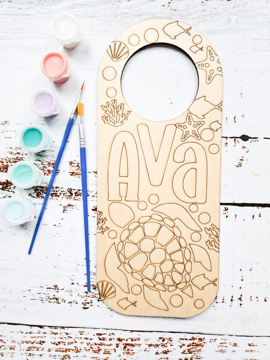 Engraved wood door hanger next to paint and paintbrushes.