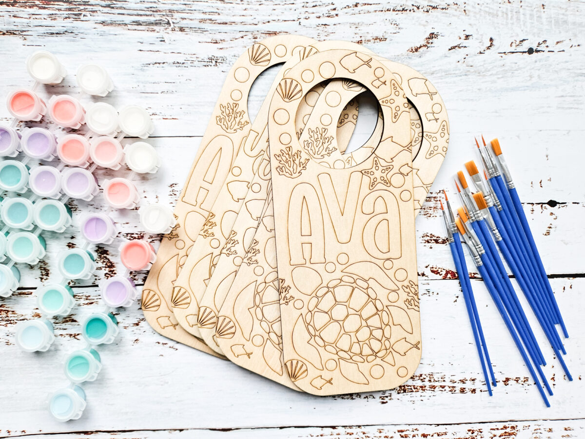 Engraved wood door hangers next to paint and paintbrushes.