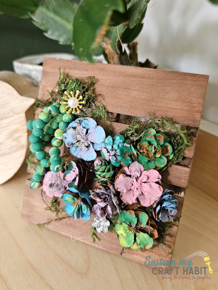 Pinecone succulent decor with embellishments on a mini pallet.