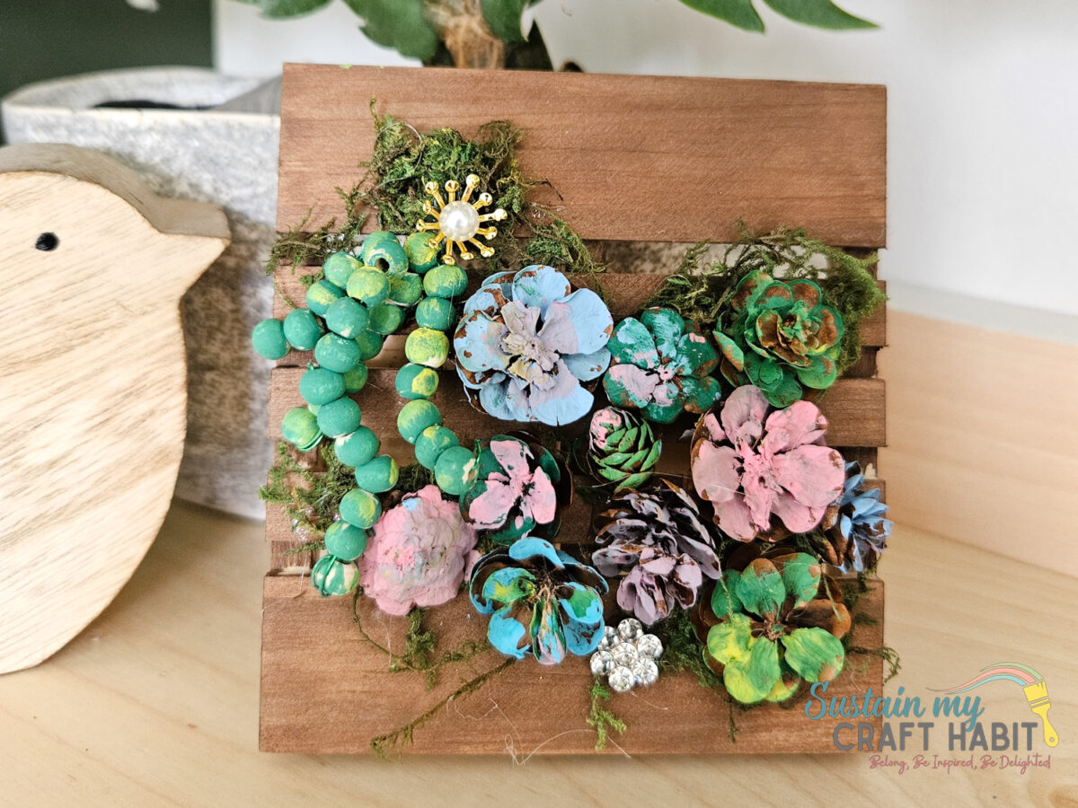 Pinecone succulent decor with embellishments on a mini pallet.